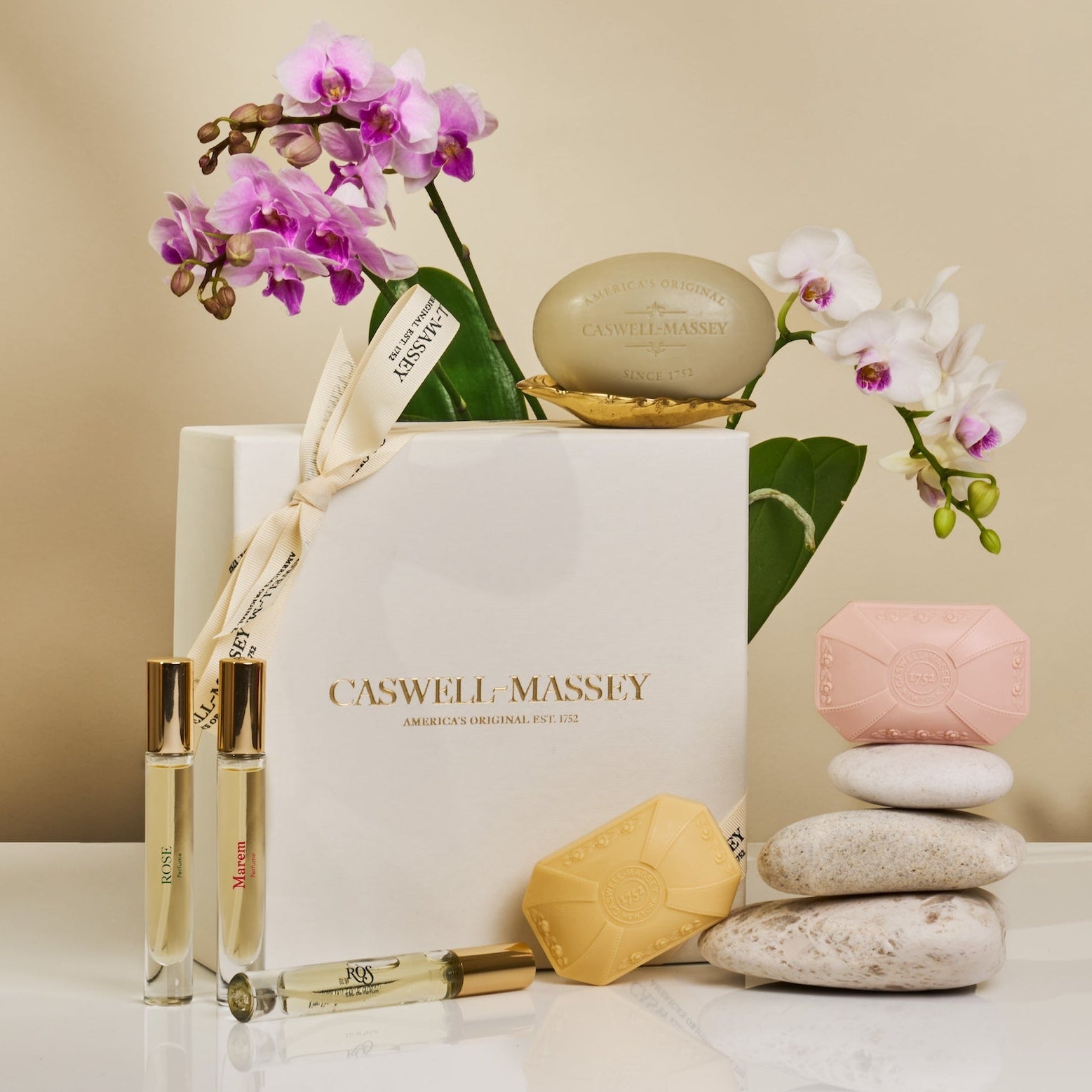 Caswell-Massey Bouquet of Roses Gift Set with flowers and stones on a beige background. Set contains 3 rose perfumes and 3 rose bar soaps.