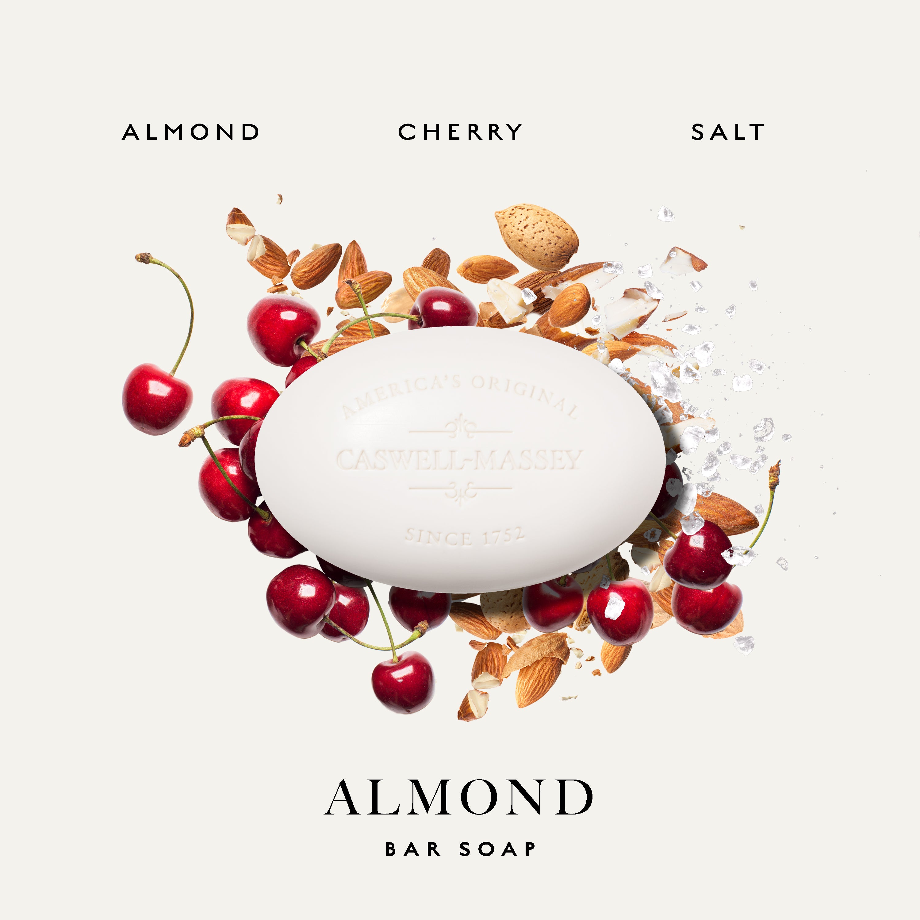 A white oval bar of Caswell-Massey Almond Bar Soap centered on a light warm gray background, surrounded by whole almonds, sliced almonds, and bright red cherries. The text 'ALMOND CHERRY SALT' appears above and 'ALMOND BAR SOAP' below the soap.