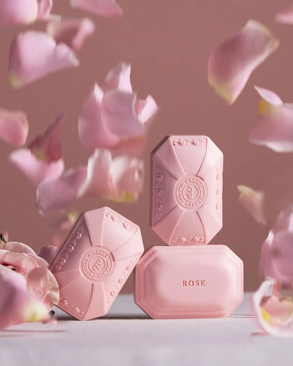 Caswell-Massey Rose Bar Soap: 3 pink bars of Rose Bar Soap shown with rose petals falling all around them.