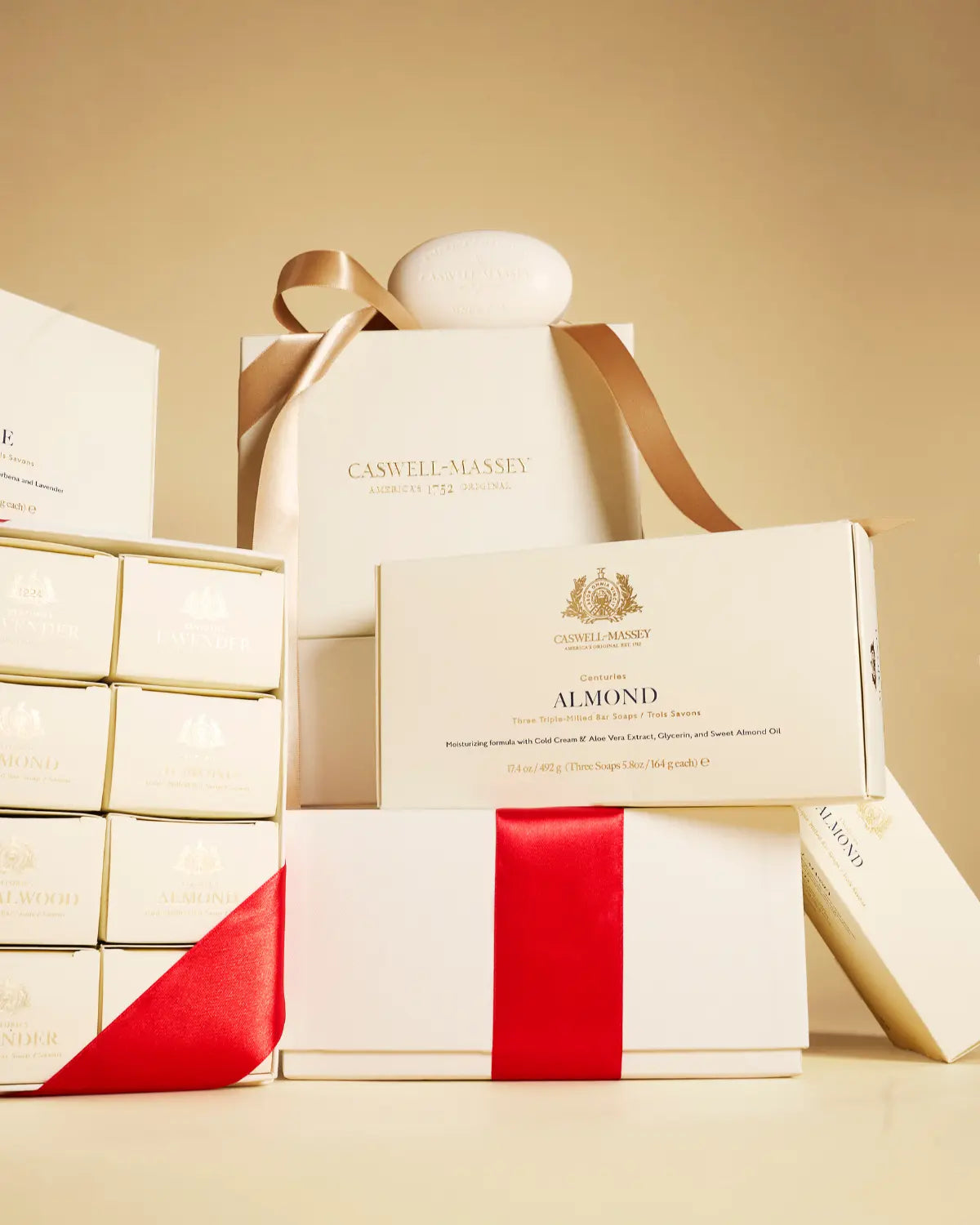Caswell-Massey Almond Bar Soap: Image shows Almond 3-Soap Sets, Almond Year of Soap Gift Sets, and Almond Single Soaps stacked together in their cream outer packaging with red ribbon.