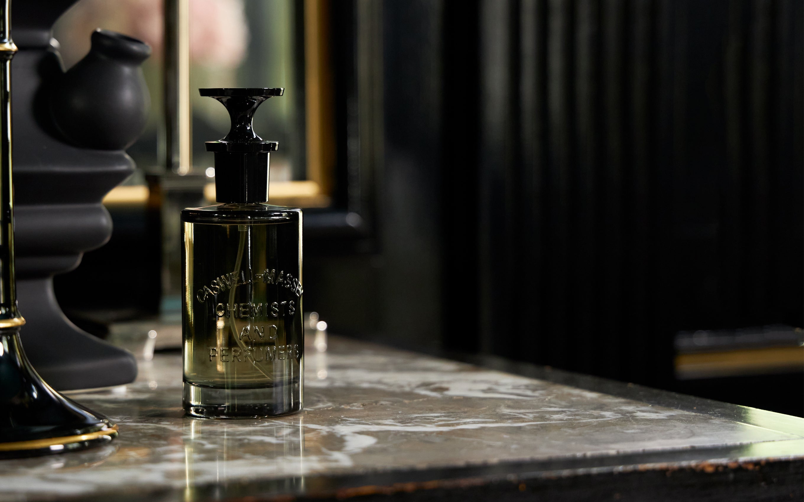 Caswell-Massey Oaire Eau de Parfum, fragrance bottle with black cap and smokey bottle sitting on dark marble tabletop