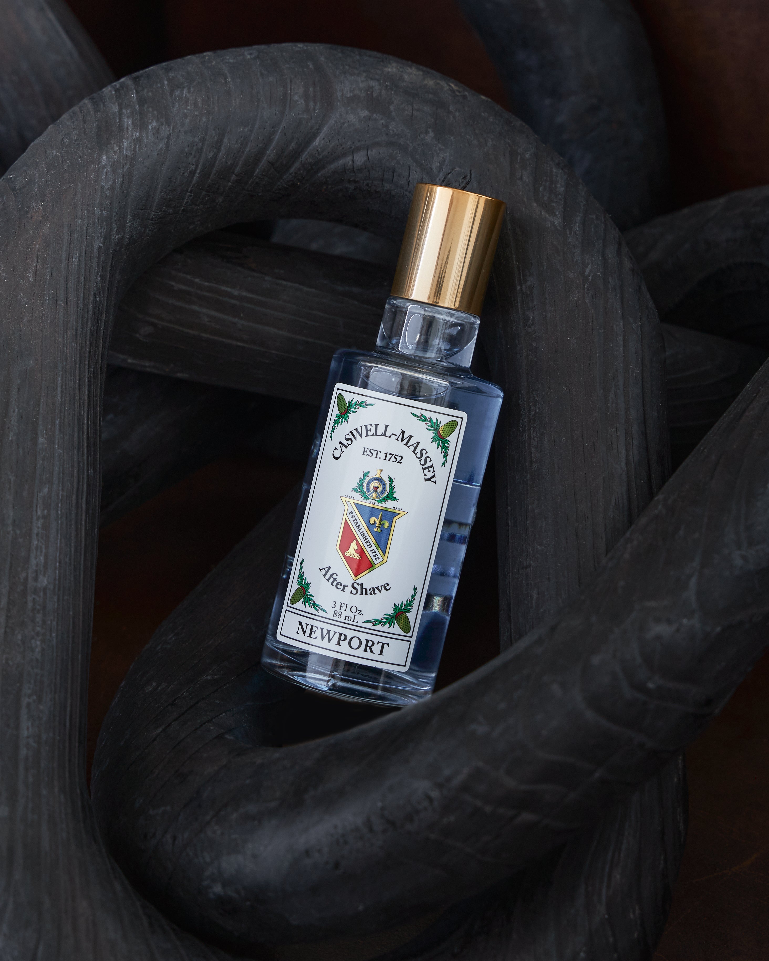 A bottle of Caswell-Massey Newport cologne with a gold cap and white label, styled on a dark textured wooden surface.