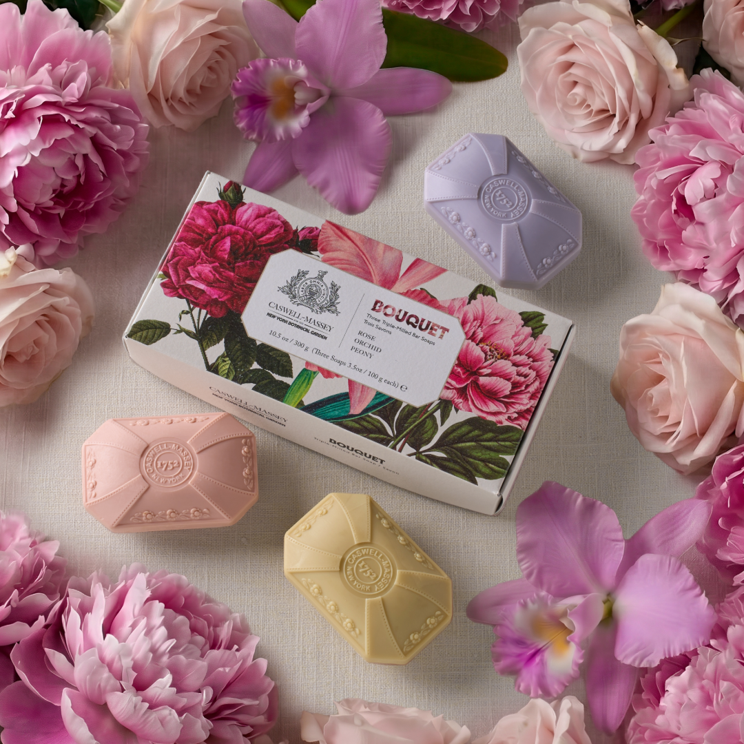 Bar soaps with floral packaging and design surrounded by pink and purple flowers on a light background