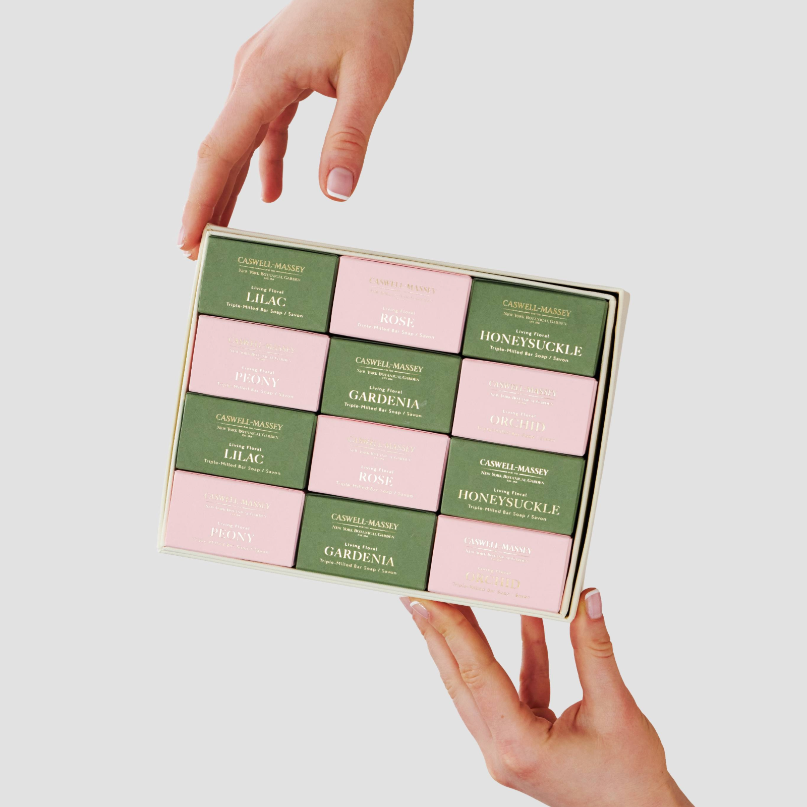 Caswell-Massey Designer Floral Year of Soap Gift Set: woman's hands holding the box open revealing the alternative pink and green color of the boxed bars of soap filling the gift box