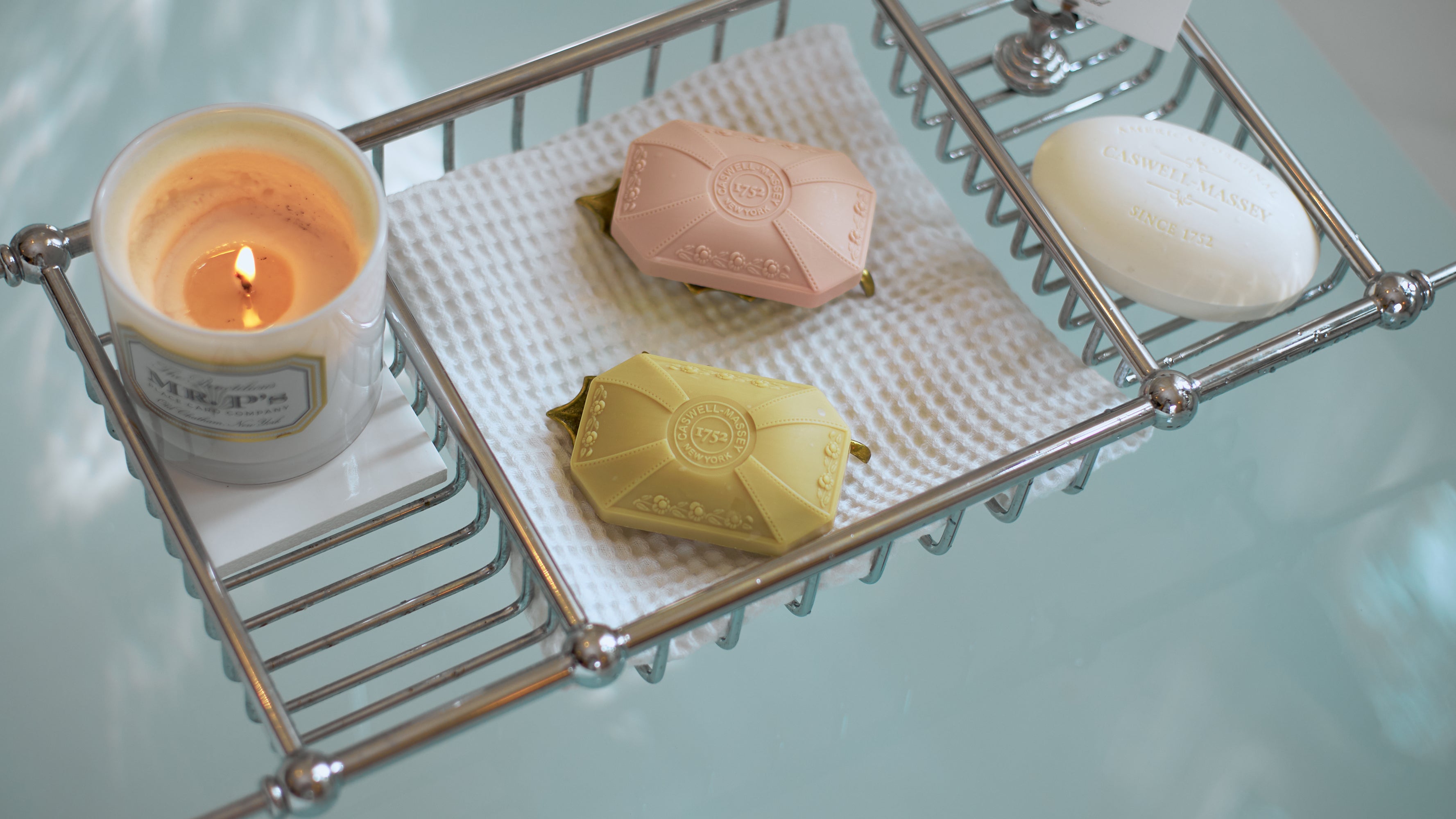 Floral scented bath soaps sitting on a bath caddy over a bathtub full of bath water from Caswell-Massey