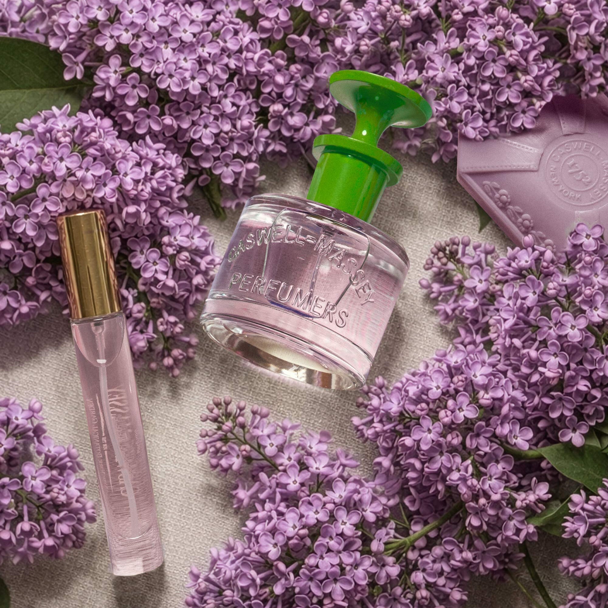 Caswell-Massey Lilac Eau de Toilette for Women. Image shows Lilac perfume with Lilac Bar Soap surrounded by fresh lilacs
