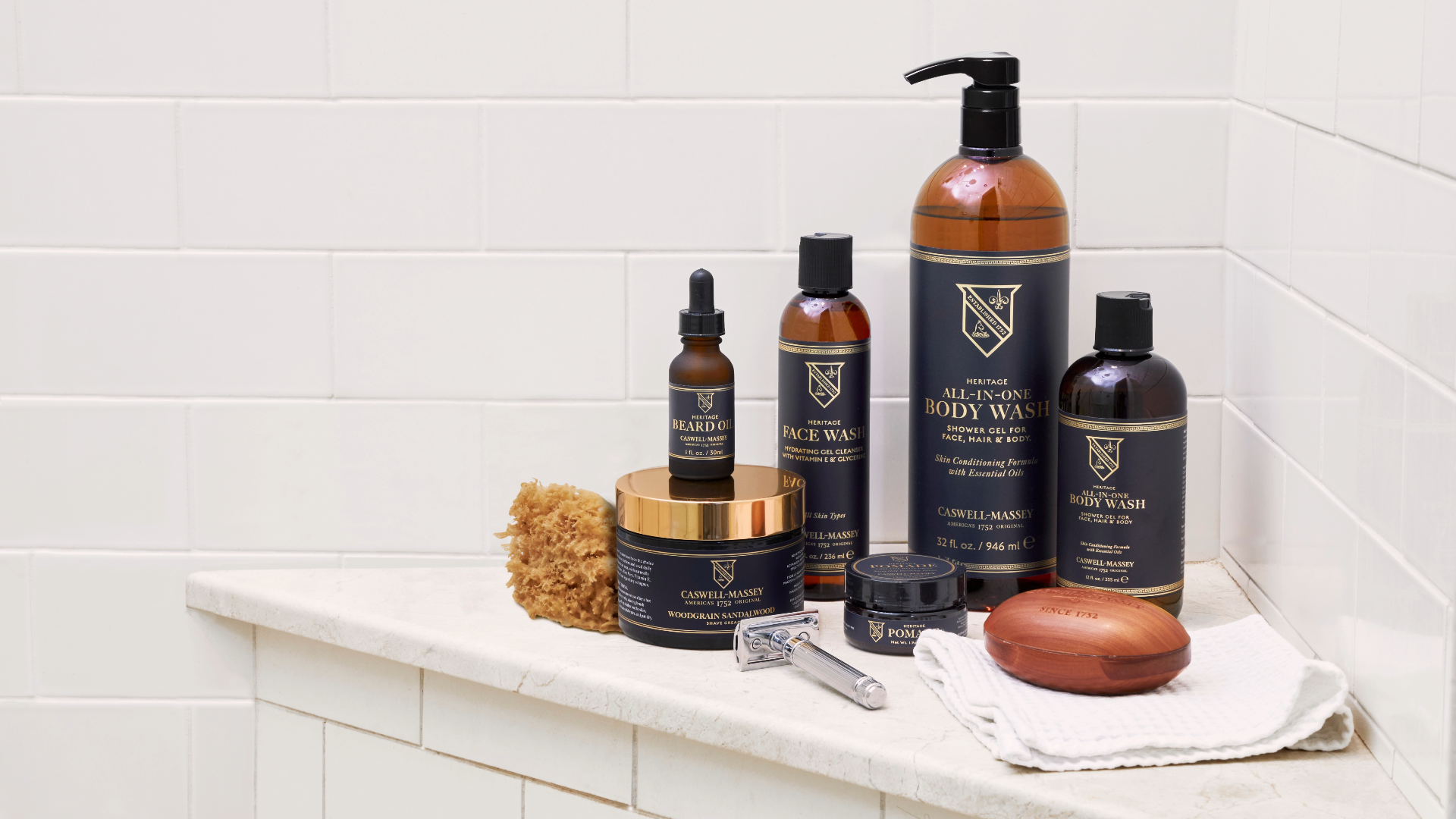 Caswell-Massey: Men's grooming and shave products on bath counter. Shave Cream, Beard Oil, Chrome Razor, Hair Pomade, Face Wash, All-in-One Body Wash, and Woodgrain Sandalwood Bar Soap