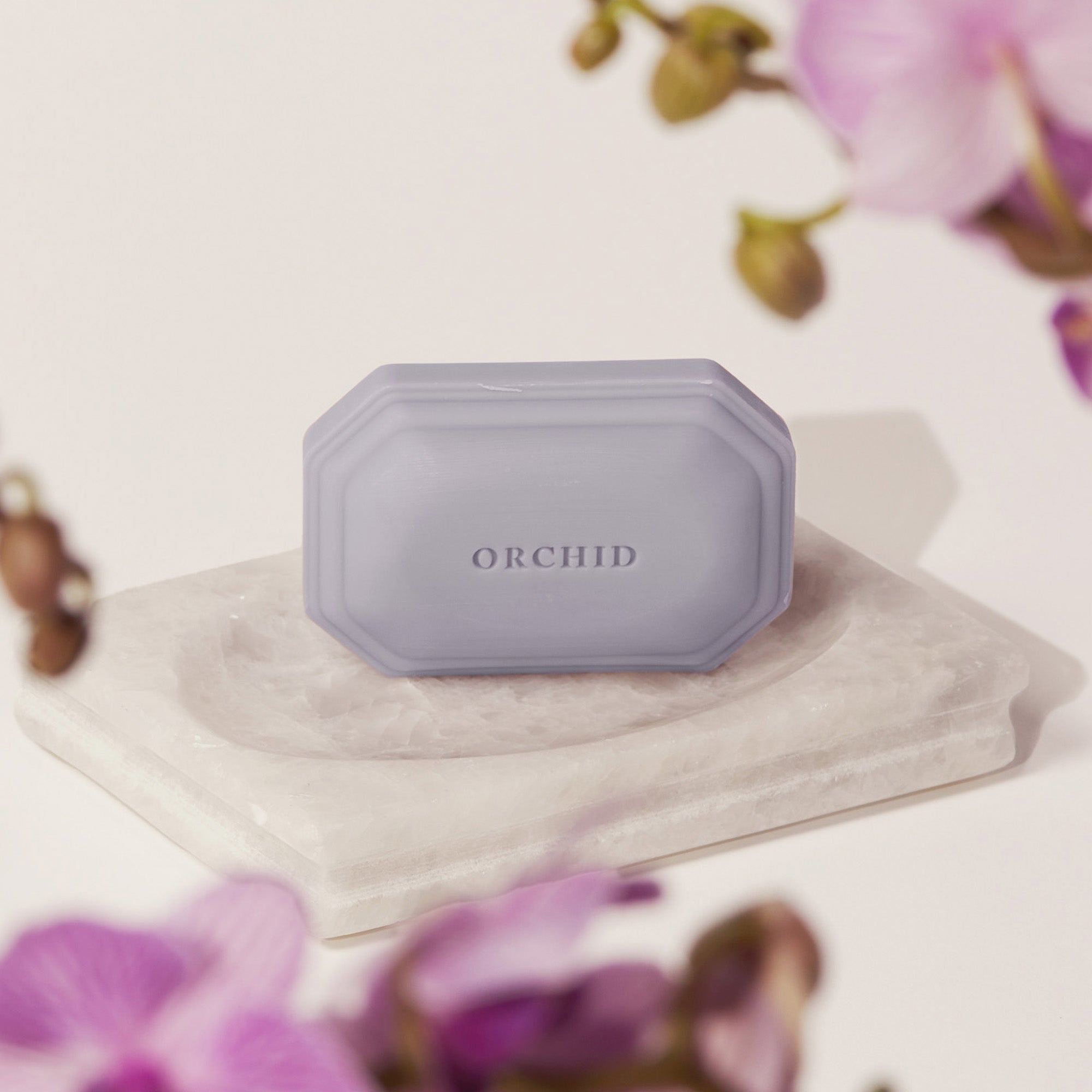Caswell-Massey Orchid Bar Soap shown on marble soap dish with purple orchid flowers