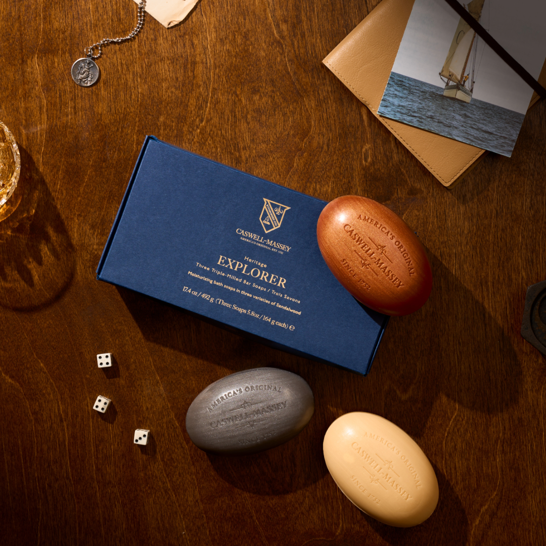 Caswell-Massey Sandalwood Explorer Bar Soap Gift Set. Three bars of soap on a wooden surface with a blue box labeled 'Explorer'
