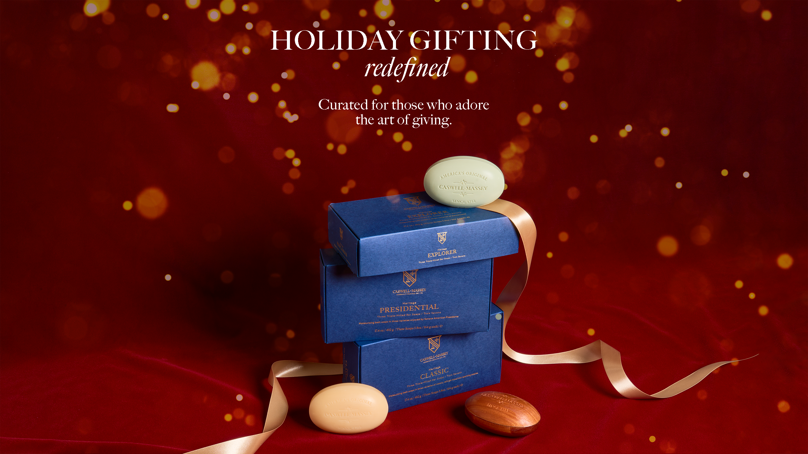 Caswell-Massey: Holiday Gifting Redefined. Curated for those who adore the art of giving. Image shows 3-soap gift set boxes stacked on top of one another against a red velvet background with gold ribbon.