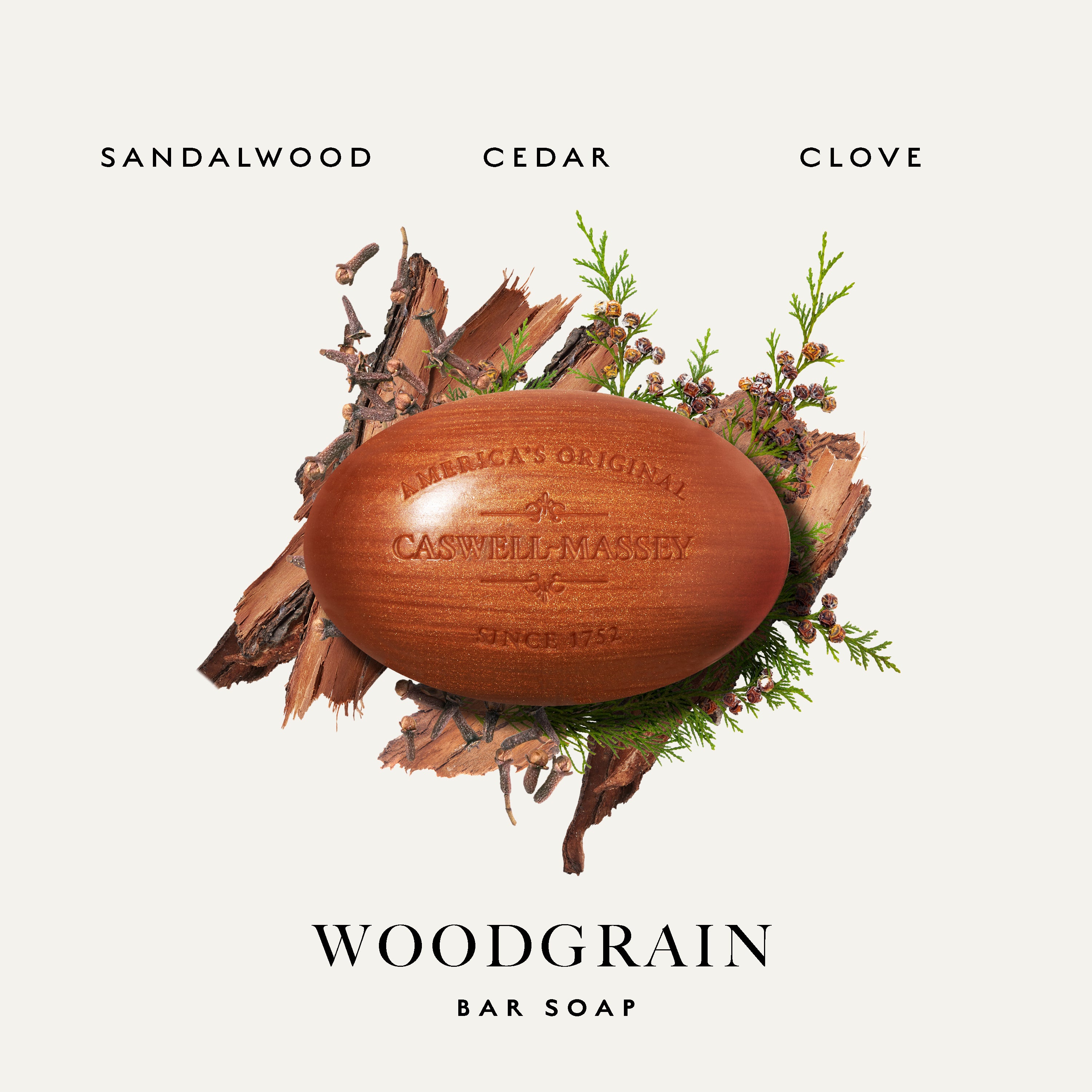 Caswell-Massey Woodgrain Bar Soap in Sandalwood, Cedar, and Clove scents, shown as a round wooden bar surrounded by bark, pine needles, and moss on a light beige background.