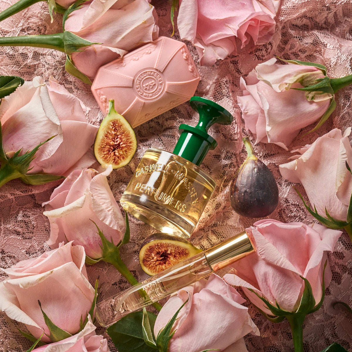 Caswell-Massey Rose Perfume. Image shows Rose Perfume bottle surrounded by fresh pink rose and fresh ripe figs to reference the scent notes of the fragrance. All objects sitting on top of a lace pink fabric.