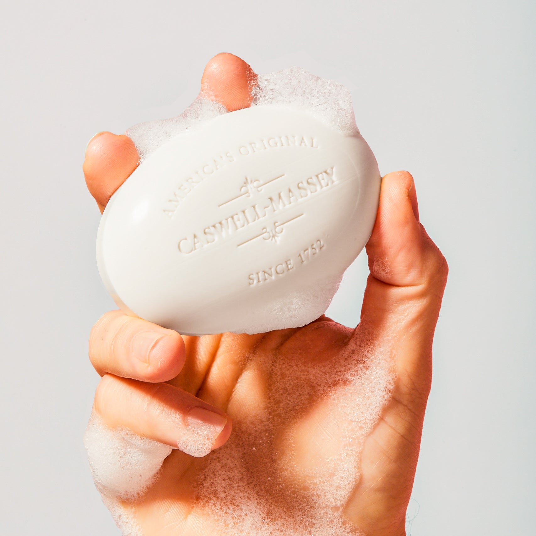 Caswell-Massey Almond Bar Soap, white bar of soap shown with rich lather in hand