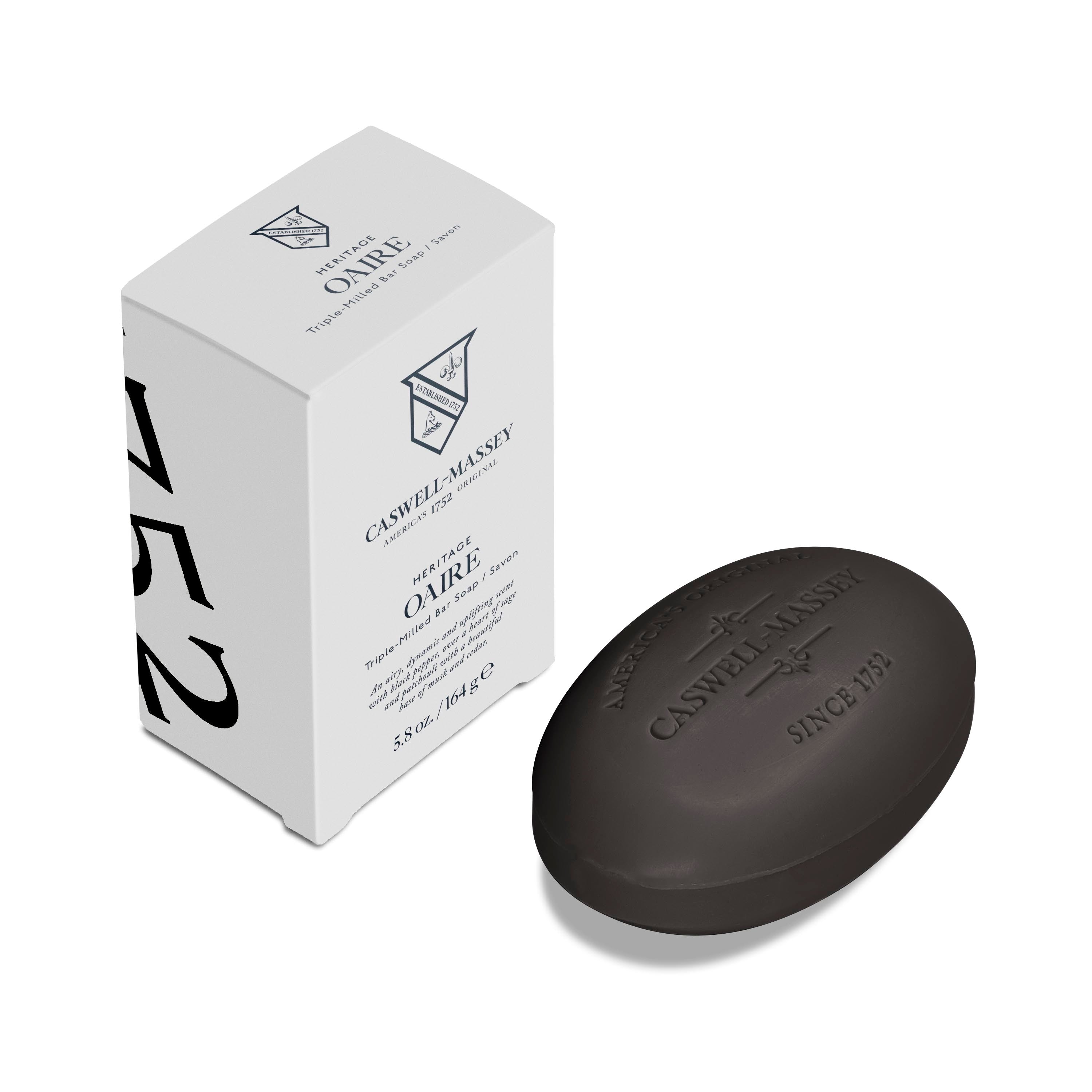 Caswell-Massey: OAIRE Black Clay Bar Soap shown as oval luxury bath soap sitting next to outer packaging of grey box