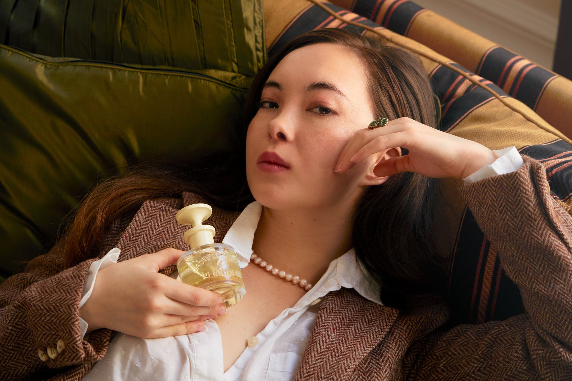 Woman reclining on sofa holding fragrance bottle