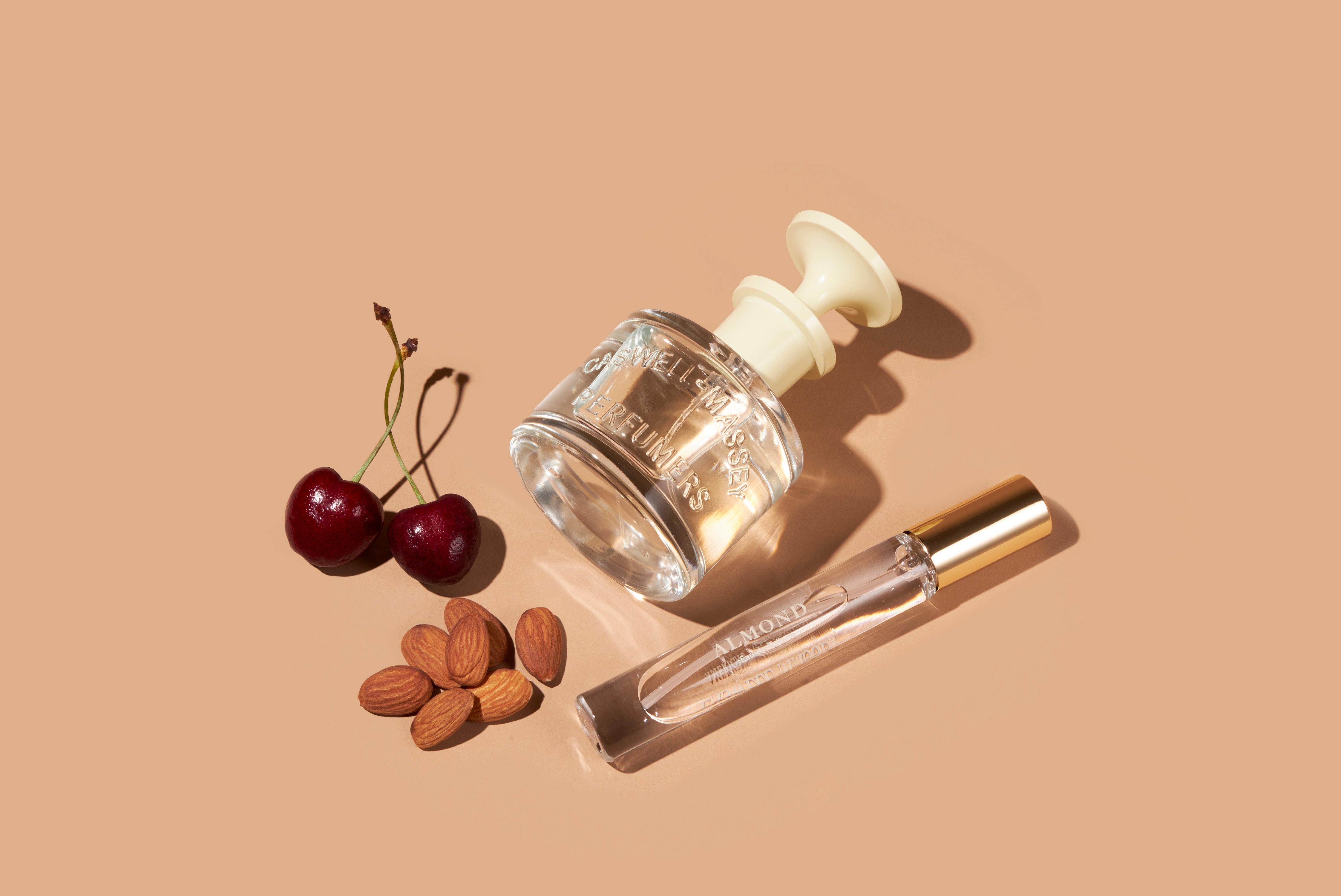 Caswell-Massey Almond Eau de Toilette, both the full-size 60ml and the travel-size 7.5ml Eau de Toilette are shown along with almonds and cherries, which reference the scent notes of this perfume.