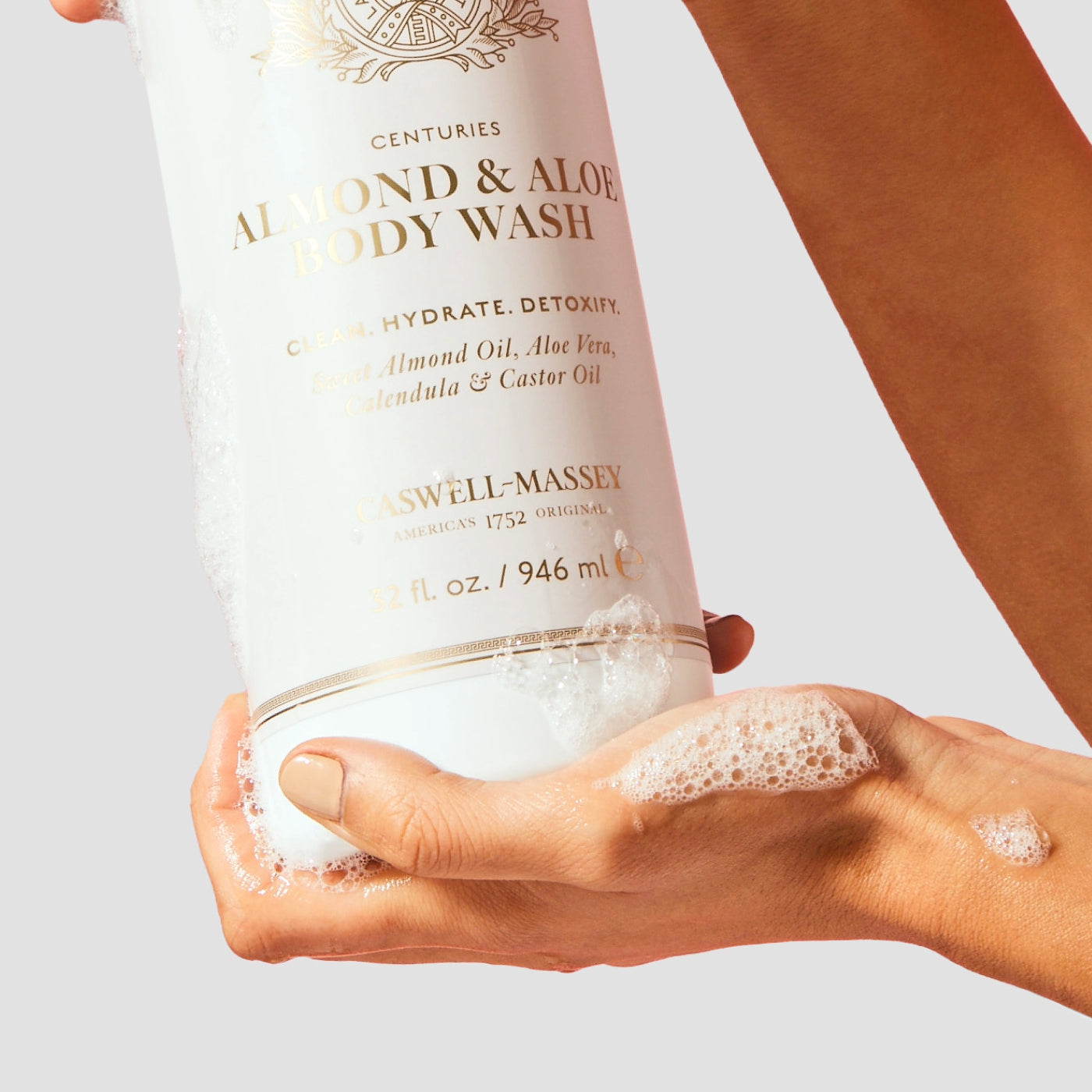 Caswell-Massey Almond & Aloe Body Wash. Image shows woman holding bottle in hand in the shower