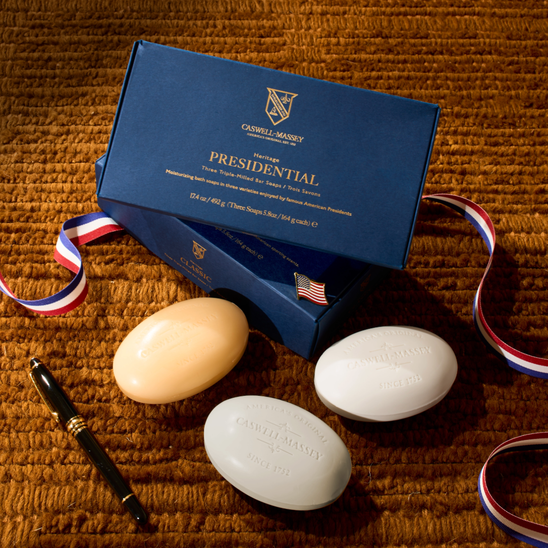 Three soaps and a box labeled 'Caswell-Massey Presidential' on a textured brown surface. Almond Bar Soap, Number Six Bar Soap, and Jockey Club Bar Soap