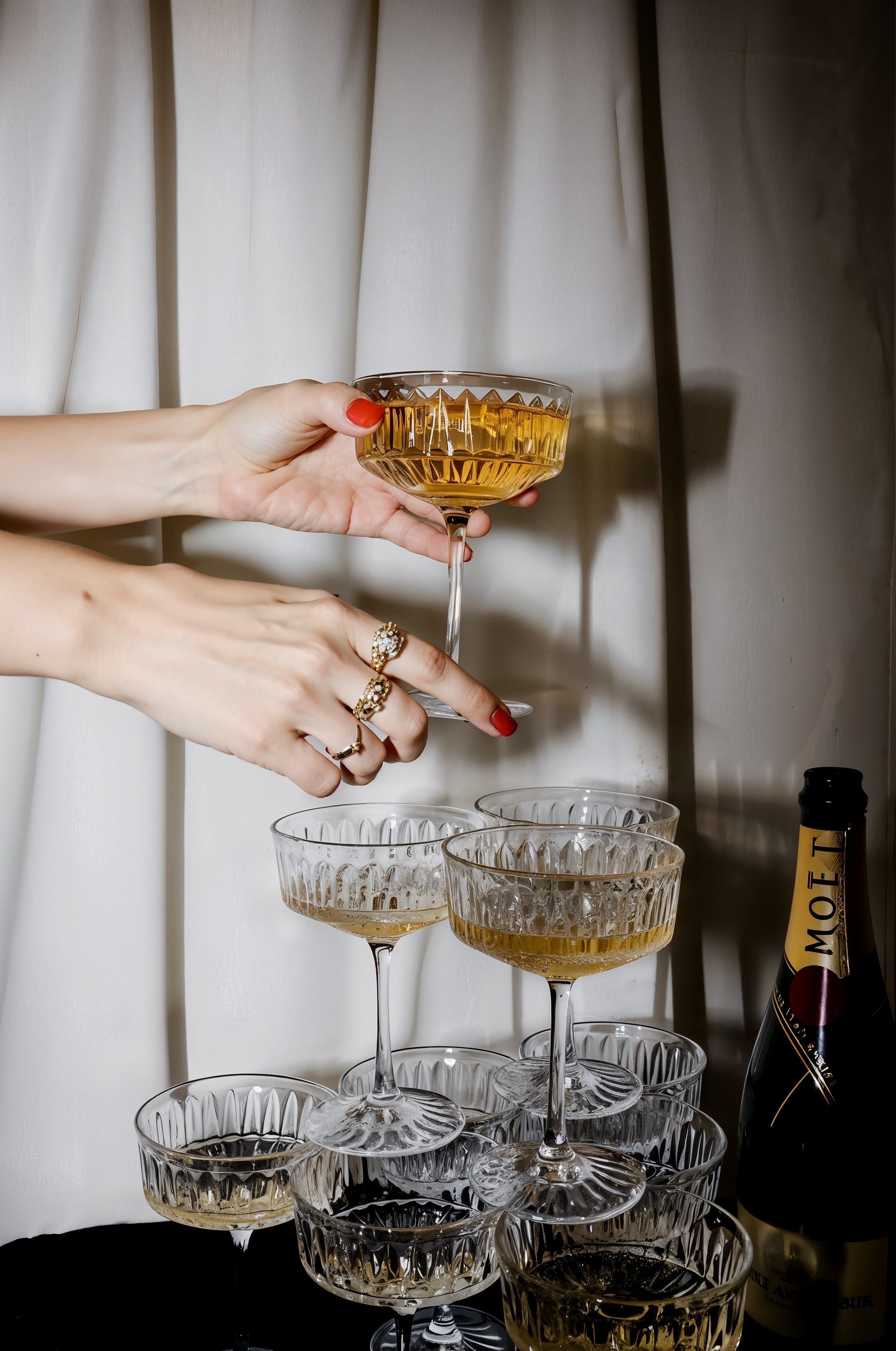 Woman's hands picking up a champagne coupe among a group of freshly poured glasses of champagne